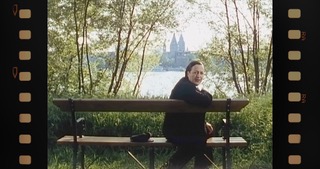 Filmstill: die Schauspielerin als Maria Einsmann auf einer Bank am Rheinufer