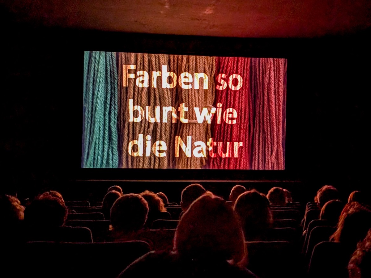 Sinema salonunda „Farben so bunt wie die Natur“ başlığının göründüğü perdenin önündeki seyirciler
